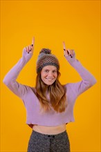 Woman with wool cap on a yellow background pointing up