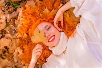 Red-haired woman lying on leaves in a park in a forest