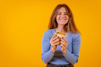 Portrait of woman eating a sandwich on a yellow background