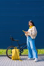 Asian college girl listening to music with yellow headphones on a blue background