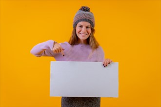 Woman in wool hat pointing at a sign on a yellow background
