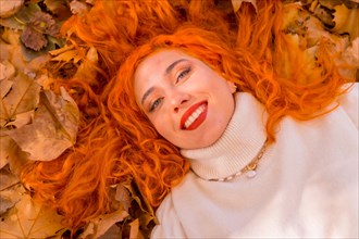Red-haired girl lying on leaves in city park