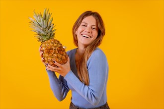 Girl smiling with a pineapple in sunglasses in a studio on a yellow background