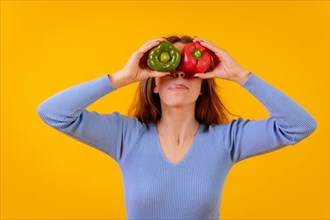 Vegetarian woman in a portrait with peppers in her eyes on a yellow background