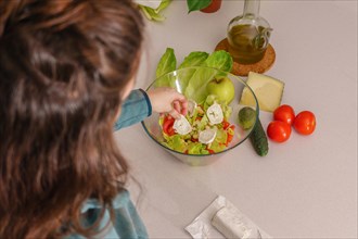 Above view of a woman adding goat cheese to a healthy salad at her kitchen table