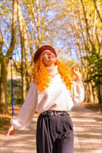 Portrait of red-haired woman in a beret walking through a city forest park at sunset