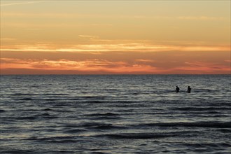 Two bathers between waves on the Baltic Sea and sunset in summer on the beach of Kloogaranna