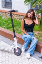 Portrait of a young brunette woman sitting in the city waiting for friends with an electric scooter