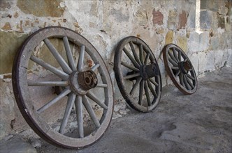 Historic old carriage wheels of carriages stand against an old sandstone wall