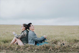 Couple in love in the field sitting back to back looking at the sky
