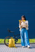 Asian college girl listening to music with yellow headphones on a blue college background