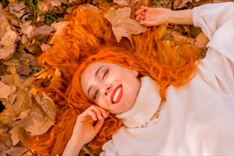 Redhead woman lying on leaves in city park smiling