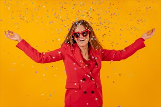 Woman smiling in red dress on a yellow background throwing with confetti