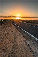 Empty asphalt road through the desert or dunes. Sunrise over the road