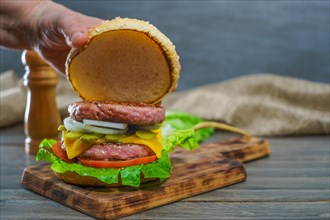 Close-up of a woman's hands opening the bun of a hamburger bun complete with two pieces of meat on a wooden board