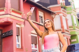 Young blonde caucasian woman in a street with houses with colorful facades smiling taking a selfie