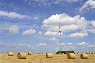Wind turbine at a stubble field with round bales of straw