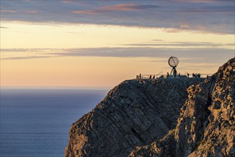 Rock cliff of the North Cape with steel globe at midnight sun