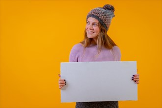 Woman in a wool cap holding a white billboard on a yellow background