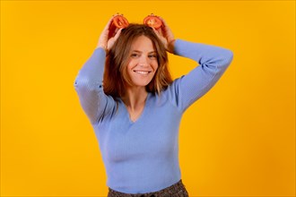 Vegan woman smiling with tomato slices on her head on a yellow background