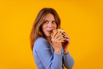 Portrait of cheerful woman eating a sandwich on a yellow background