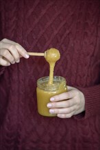 Hands holding honey jar with honey spoon