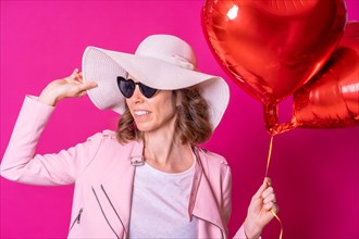 A blonde caucasian woman with a white hat and sunglasses in a nightclub with some heart balloons