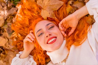 Red-haired woman lying on leaves in a park in a forest