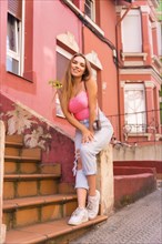 Portrait of young blonde caucasian woman in a street with houses with pink colorful facades
