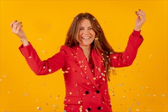 Woman having fun in red dress on a yellow background throwing with confetti