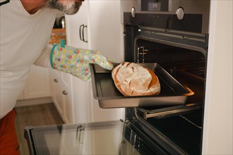 Older man with beard putting bread in the oven of his house