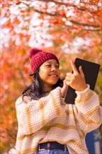 Asian girl walking in autumn with a tablet in her hand in a forest of red leaves