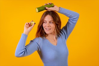 Portrait of a vegan woman holding a cut cucumber on a yellow background