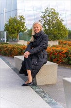 Corporate portrait of middle aged businesswoman sitting outside of office skyscraper