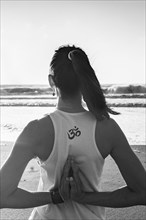 Rearview shot of a young woman practicing yoga at the beach. Om sign. Black and white shot