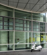 White Vespa scooter in front of glass facade of an office complex
