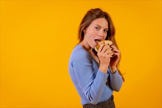 Cheerful woman eating a sandwich on a yellow background