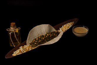 Taco with spinach and pine nuts bowl with cheese sauce and several types of cheese as garnish bottle of olive oil and black background