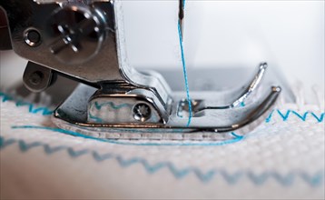 Close-up of sewing machine needle with blue thread sewing on a white fabric