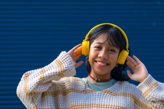 Asian young woman having fun listening to music with yellow headphones on a blue university background