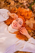 Redhead woman lying on leaves in a forest park