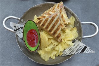 Ham and cheese toast with chips and ketchup served in a metal bowl