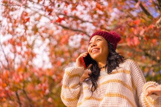 Portrait of an Asian woman in autumn with a mobile phone calling in a forest of red leaves