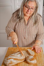 White-haired woman cutting slices of freshly baked homemade bread