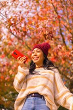 Asian girl in autumn with a mobile smiling sending a voice message in a forest of red leaves