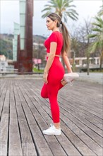 Fit woman in red outfit doing stretching in a city park
