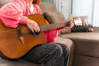 Woman playing the guitar at home sitting on the sofa in her living room next to the sale