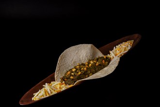 Taco with spinach and pine nuts and various types of cheeses as garnish and black background