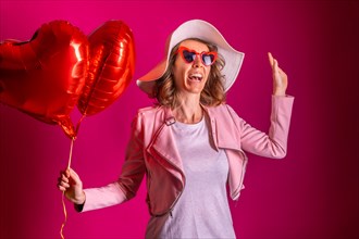 A caucasian woman enjoying dancing with a white hat in a nightclub with some heart balloons