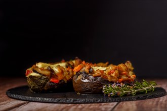 Foreground eggplant stuffed with meat and vegetables covered with bechamel sauce on a black slate on a wooden table